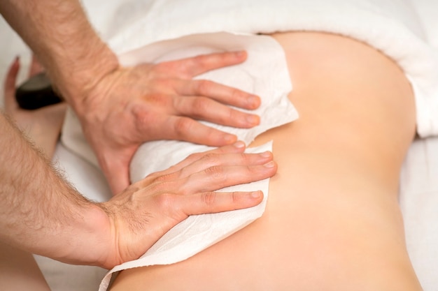 Hände eines Masseurs mit Handtuchmassage zurück einer jungen erwachsenen Frau im Spa-Salon