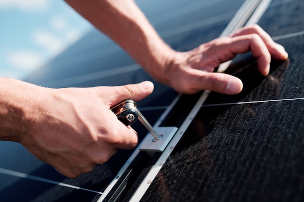 Hände eines professionellen Technikers oder Ingenieurs, der Schrauben verwendet, während Sonnenkollektoren auf dem Dach des Hauses installiert werden