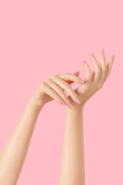 Hände eines schönen, gepflegten, beigefarbenen, nackten Marmordesign-Nagellacks auf rosafarbenem Hintergrund