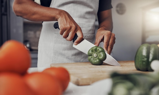 Hände Essen und Kochen mit einem Mann, der einen grünen Pfeffer in der Küche auf einem hölzernen Schneidebrett schneidet Salatgesundheit und Ernährung mit einem männlichen Koch, der eine Mahlzeit zubereitet, während er allein in seinem Haus steht