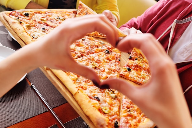 Hände falteten sich in Form einer Herznahaufnahme auf dem Hintergrund der frischen heißen Pizza