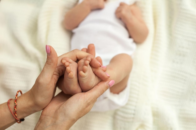 Hände halten die Beine eines kleinen schlafenden Babys auf einer weißen Decke