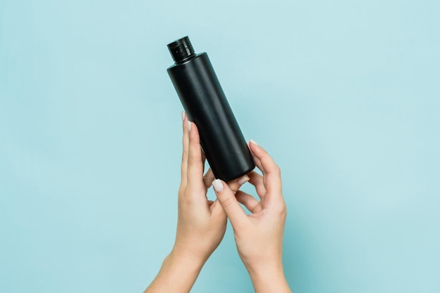 Hände halten eine schwarze Flasche Kosmetikprodukt für die Haut auf blauem Hintergrund