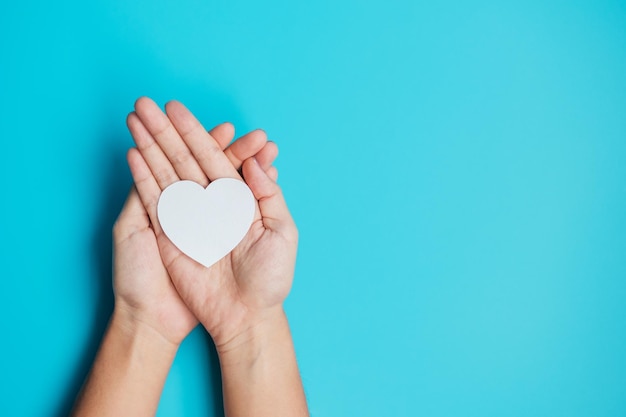 Hände halten Papier Herz auf blauem Hintergrund Spende Wellness Welt Herztag Weltgesundheitstag und Happy Valentines Day Konzepte