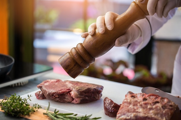 Foto hände halten pfeffermühle. grünes kraut und rohes fleisch. gewürz für kalb. zubereitung der mahlzeit im restaurant.