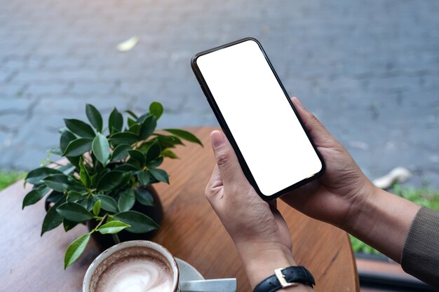 Hände halten schwarzes Handy mit leerem Desktop-Bildschirm im Café