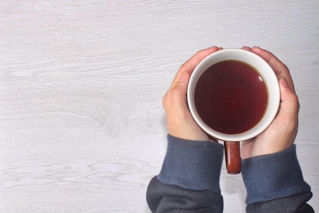 Hände halten Tasse Kaffee auf weißem Holztisch