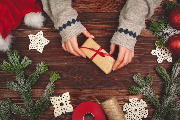 Hände im Pullover halten ein Geschenk auf Holztisch mit Weihnachtsschmuck