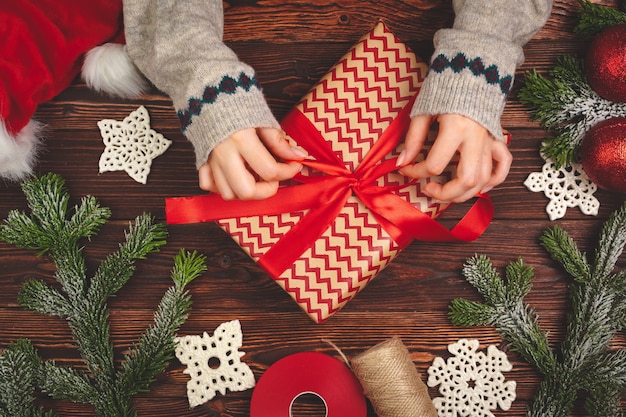 Hände im Pullover halten ein Geschenk auf Holztisch mit Weihnachtsschmuck