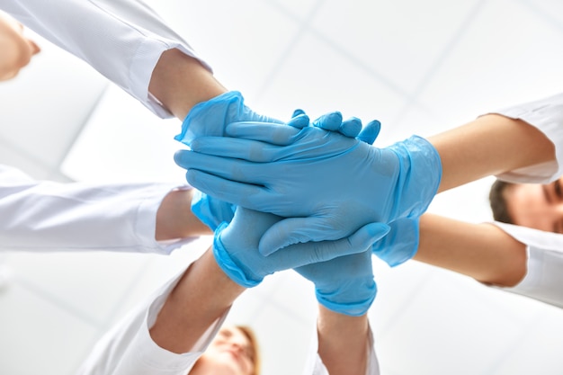 Hände in blauen Handschuhen Covid, Konzept - Kreativteam mit Händen übereinander. Vielfältiges Team, das ihre Hände zusammenlegt. Eine für alle Geste in Handschuhen. Covid-19-Konzept.