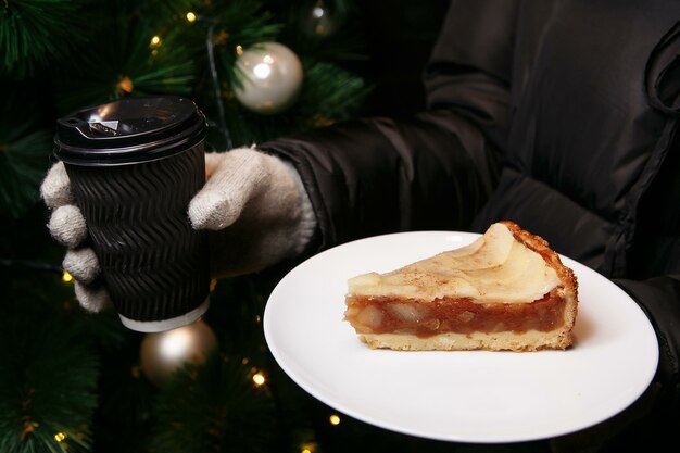 Hände in Handschuhen halten eine Tasse heißen Kaffee und ein Stück Kuchen