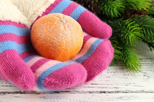 Hände in Handschuhen halten Mandarine auf Holztisch