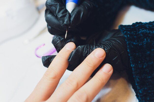 Hände in Handschuhen kümmern sich um die Handnägel des Mannes. Maniküre-Schönheitssalon.