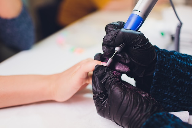 Hände in Handschuhen kümmern sich um die Handnägel des Mannes. Maniküre-Schönheitssalon.