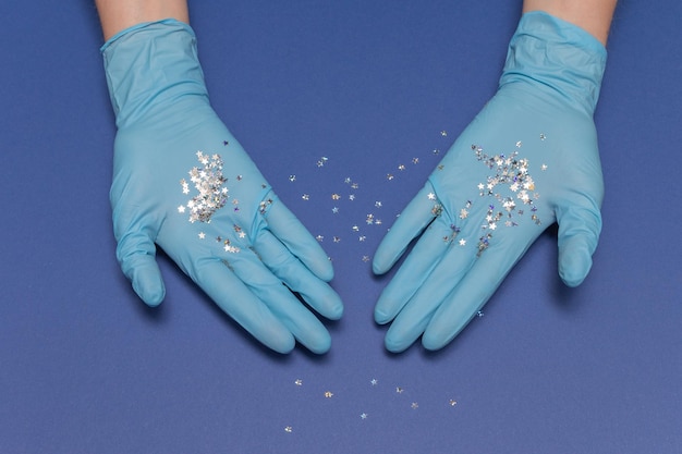 Hände in medizinischen Handschuhen auf blauem Hintergrund. Glitzernde kleine Sterne in den Händen. Weihnachten und Neujahr