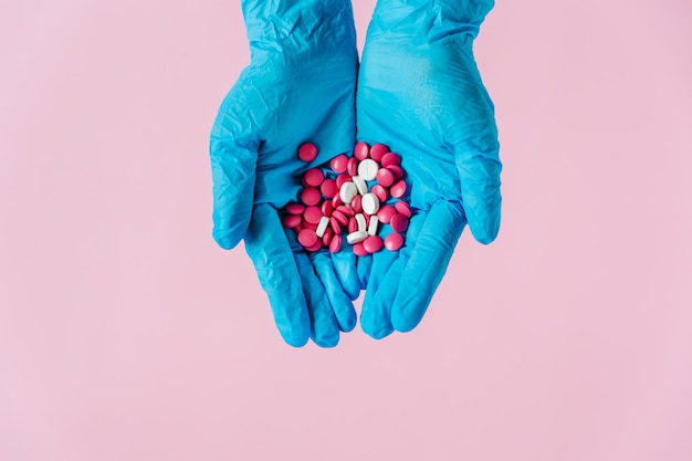 Hände in medizinischen Handschuhen mit Pillen Rosa Hintergrund Medizinisches Konzept Draufsicht Platz für Text