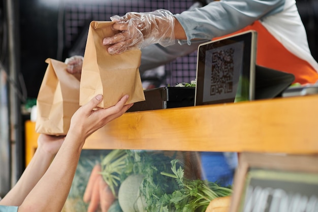 Hände in Schutzhandschuhen einer jungen Verkäuferin, die ein Papierpaket vorbeireicht