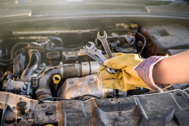 Hände in Schutzhandschuhen mit Schraubenschlüssel gegen Automotor