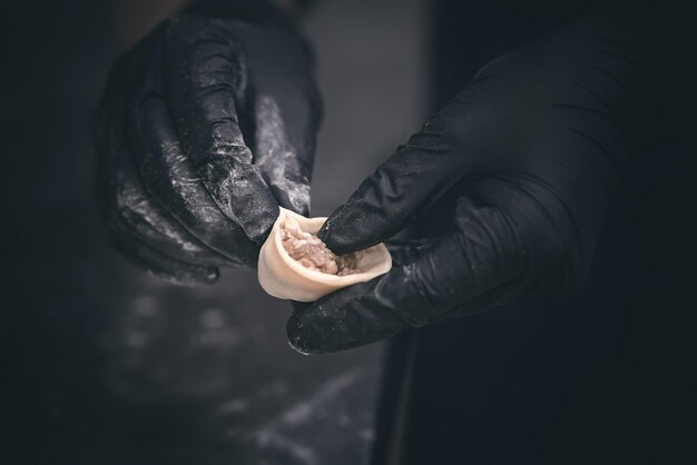 Hände in schwarzen Handschuhen formen Knödel in Nahaufnahme mit geringer Schärfentiefe