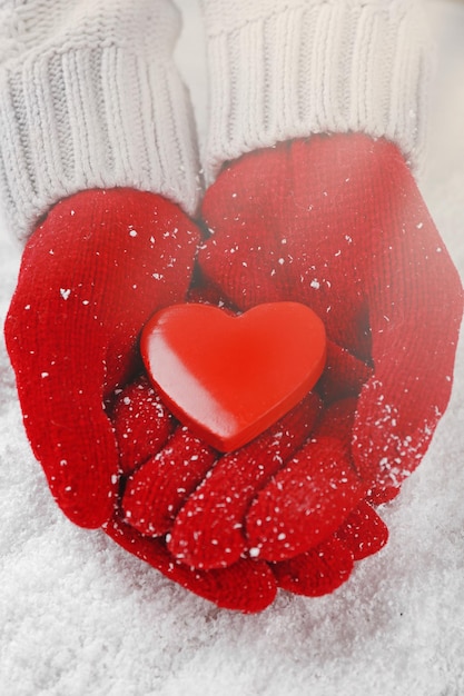 Hände in warmen roten Handschuhen, die Herz auf schneebedecktem Hintergrund halten