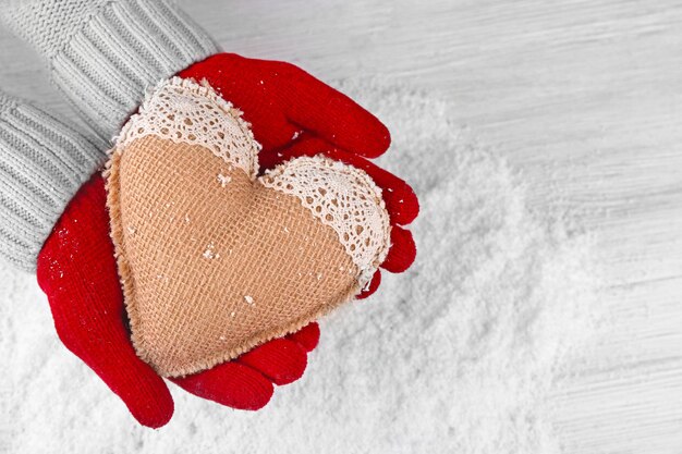 Hände in warmen roten Handschuhen, die Stoffherzen auf schneebedecktem Hintergrund halten