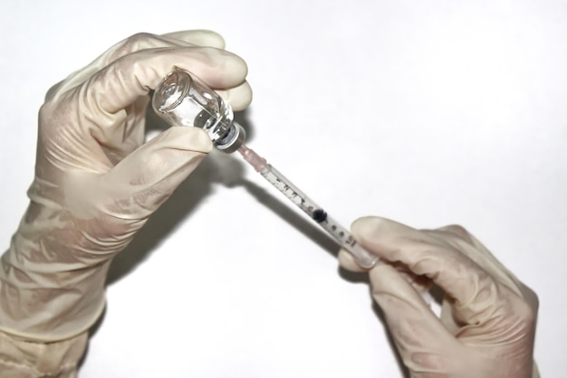 Hände in weißen Handschuhen, die Spritze und Glasfläschchen halten, bereiten sich auf die Injektion vor