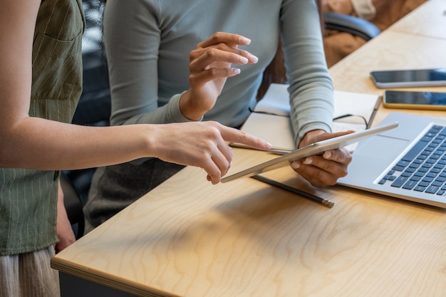 Hände junger Geschäftsfrauen in Freizeitkleidung, die Informationen auf dem Bildschirm des digitalen Tablets diskutieren, während sie sich auf die Konferenz am Schreibtisch vorbereiten