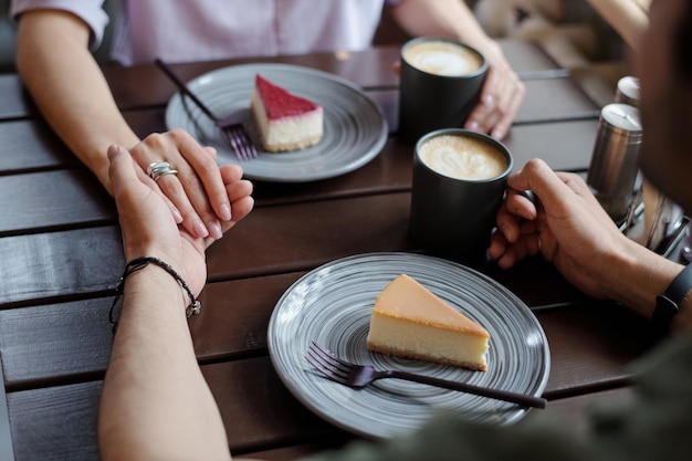 Hände junger liebevoller Datteln mit Cappuccino-Tassen am Tisch