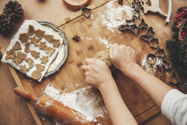 Hände kneten Teig für Lebkuchenplätzchen auf rustikalem Tisch auf dem Hintergrund von hölzernen Nudelholzplätzchen Metallschneider Weihnachtsdekorationen Prozess der Herstellung von Keksen mit der Familie