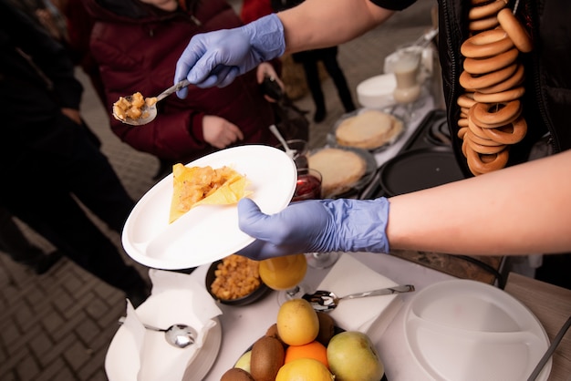 Hände Köche in blauen Handschuhen halten einen Teller Pfannkuchen und verhängen eine Füllung. Pfannkuchenwoche