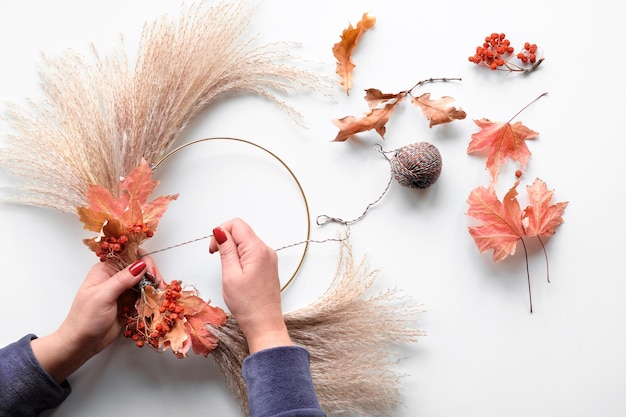 Hände machen getrockneten Blumenkranz aus trockenem Pampasgras und Herbstlaub Hände in Pullover-Krawatten-Dekorationen an Metallrahmen