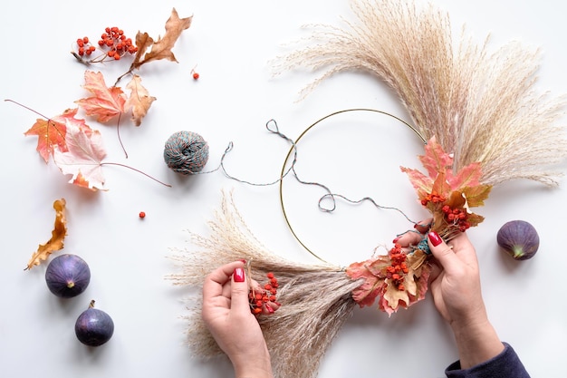 Hände machen getrockneten Blumenkranz aus trockenem Pampasgras und Herbstlaub Hände in Pullover-Krawatten-Dekorationen an Metallrahmen