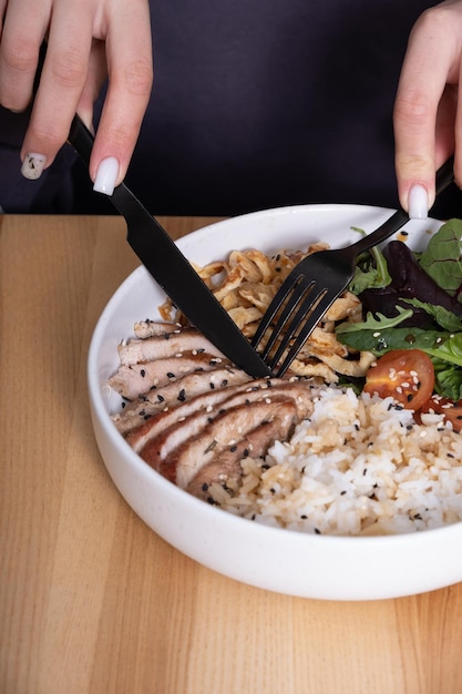 Hände mit Geschirr über einer Schüssel mit Fleisch, Reis und Gemüse