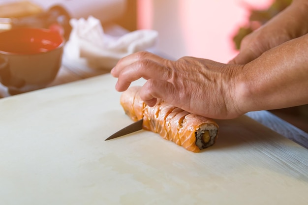 Hände mit Messer schneiden Sushi. Sushi rollt auf Kochbrett. Traditionelles Uramaki-Sushi mit Lachs. Neues Rezept vom Küchenchef.