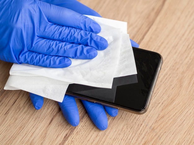 Foto hände mit op-handschuhen, die das smartphone desinfizieren