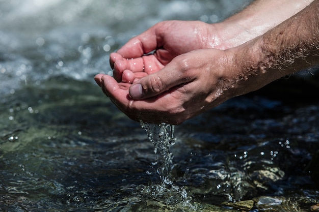 Hände mit sauberem Wasser aus dem Gebirgsbach sprudeln