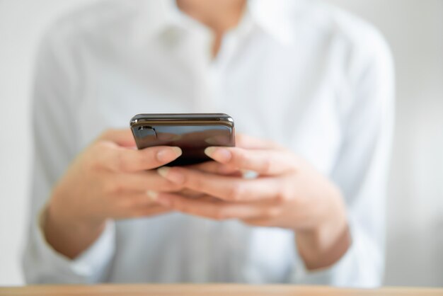 Hände mit Smartphone auf Holztisch und Nachricht an seine Freunde eingeben.