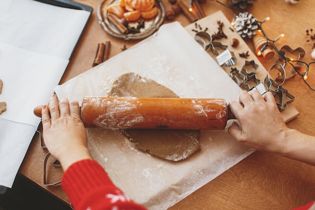 Hände rollen rohen Lebkuchenteig mit Nudelholz auf rustikalem Tisch Weihnachtskekse machen