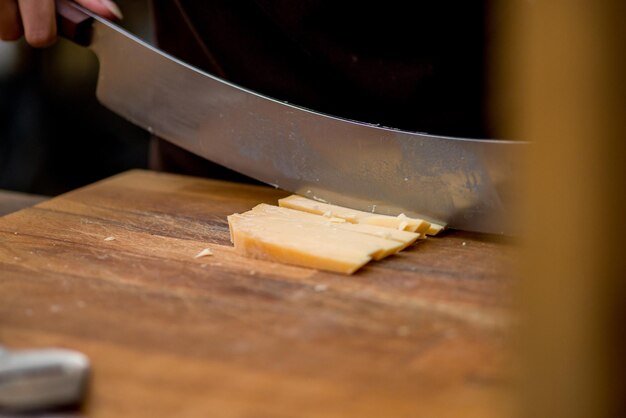 Hände schneiden den Käse mit einem speziellen Messer in Stücke