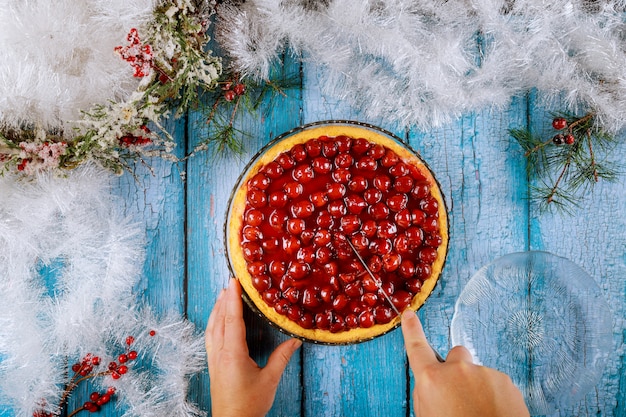 Hände schneiden Kirschkuchen auf blauem Holztisch