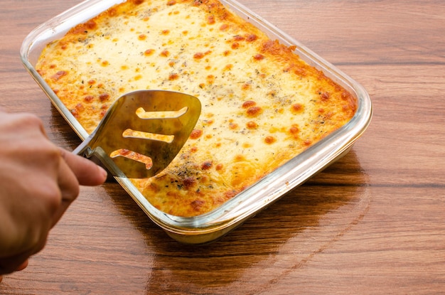 Hände schneiden Lasagne auf Glasplatte Kochkonzept Zusammensetzung des Kochens von Lasagne auf Holz.