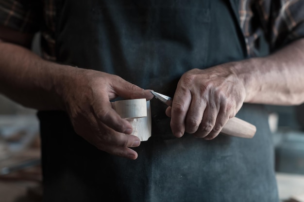 Hände schnitzen Tasse aus Holz, arbeiten mit Meißel aus nächster Nähe. Werkstatt aus Holz. Verfahren zur Herstellung von Küchengeschirr aus Holz Hochwertiges Foto