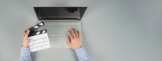 Hände tippen und Computer-Laptop oder Notebook mit schwarzer Klappe oder Filmtafel auf grauem Hintergrund. Studioaufnahme. Top-Eye-Ansicht.