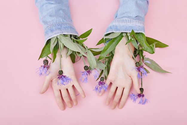 Hände und Frühlingsblumen sind auf einer rosa Tabellenhautpflege. Naturkosmetik