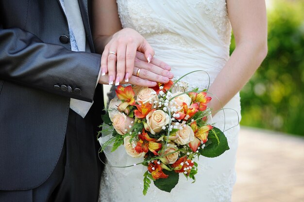 Hände und Ringe auf Hochzeitsorangenblumenstrauß