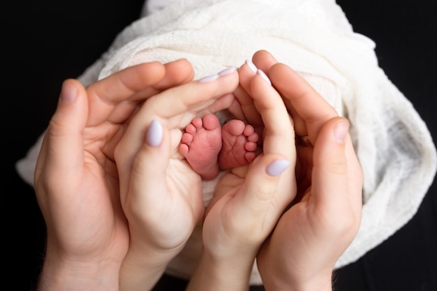 Hände von Eltern und Kindern. Beine eines Neugeborenen in den Händen von Mama und Papa. die Beine des Babys in den Händen.