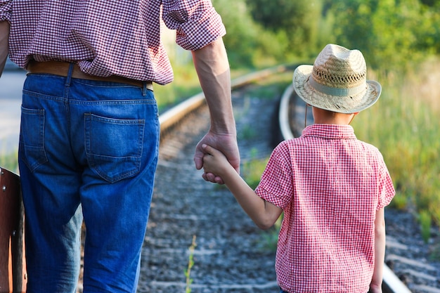 Hände von Elternteil und Sohn in Cowboyhut in der Nähe der Eisenbahn mit Koffer