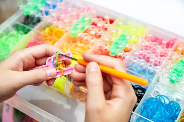 Hände von Mädchen weben Armband aus Gummibändern