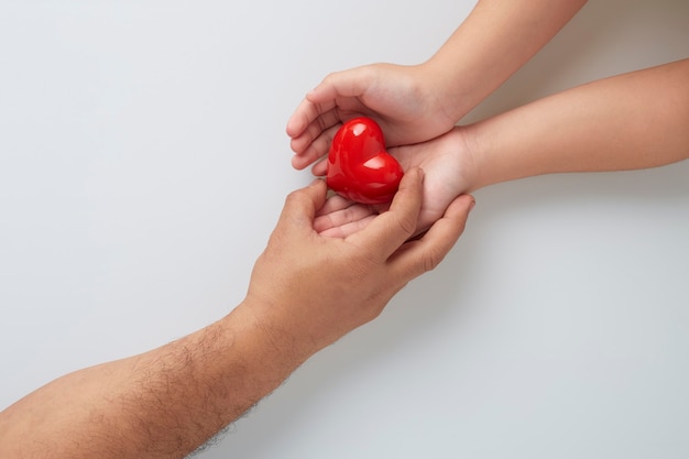 Hände von Mann und Kind mit einem roten Herzen auf weißer Wand