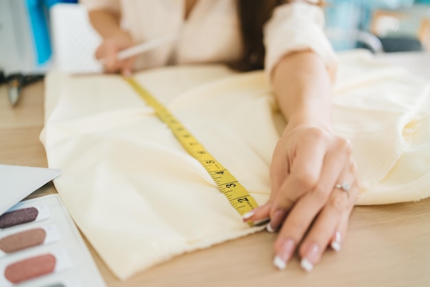 Hände von Modedesignerinnen oder Schneiderinnen messen Papier mit Maßband für die Herstellung von Kleidungsmustern Modedesigner-Schneider in der Werkstatt, die für eine neue Kollektion arbeitet